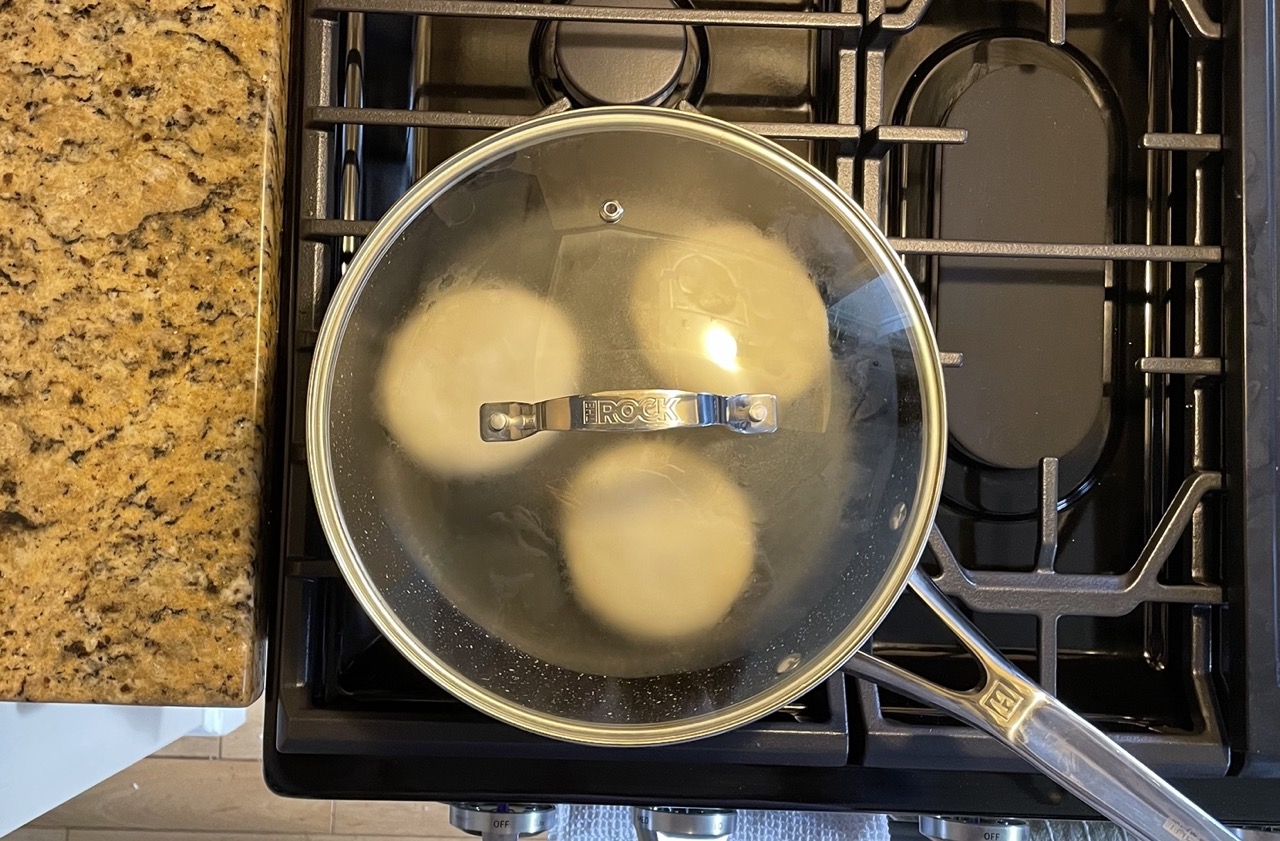 shows the english muffins in the pan with a lid on