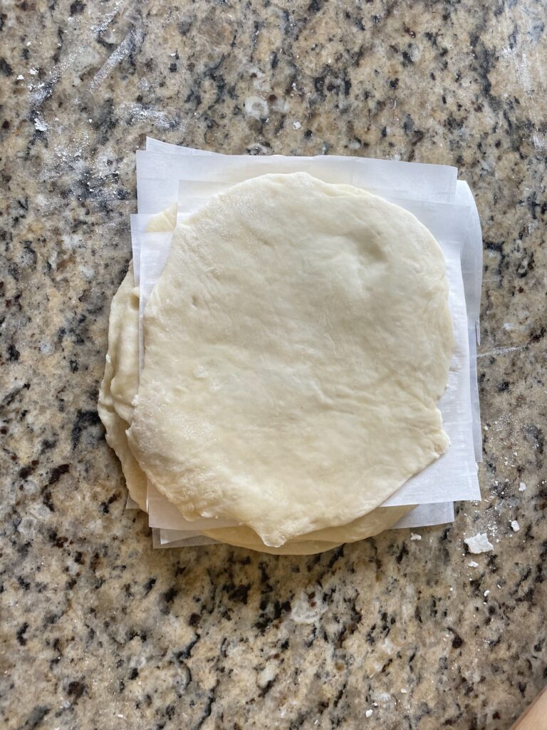 This image shows the dough balls rolled with a rolling pin and stacked on top of eachother with parchment paper in between