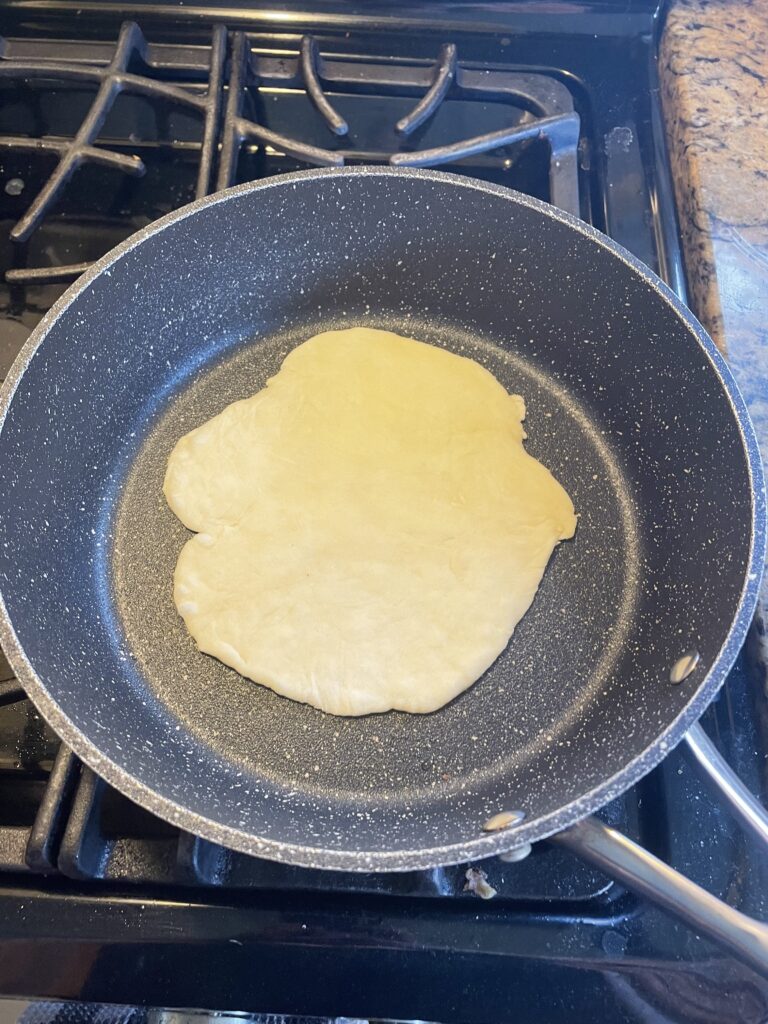 This image shows a singular tortilla cooking in a pan on the stove